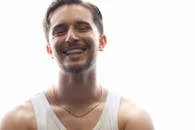 Bright portrait of a smiling young man in a white tank top with a casual gold chain.